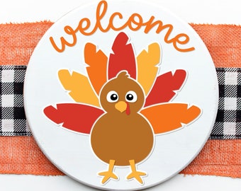 May include: A white round sign with the word "welcome" written in a brown cursive font. A cartoon turkey with orange, red, and yellow feathers is in the center of the sign. The turkey has brown feathers, a red wattle, and large black eyes.