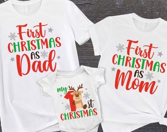 May include: Three white t-shirts with red and green text. The first shirt says "First Christmas as Dad". The second shirt says "First Christmas as Mom". The third shirt says "My First Christmas".