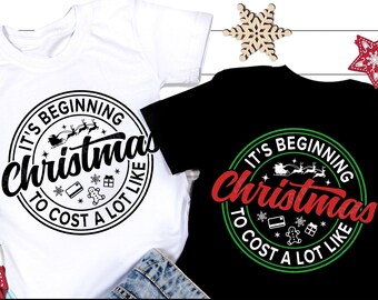 May include: Two white and black t-shirts with a green and red circle design. The design says "It's Beginning to Cost a Lot Like Christmas".