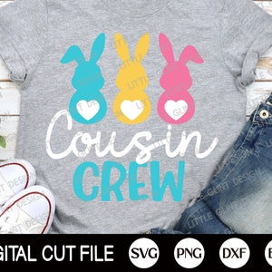May include: A grey t-shirt with a design of three Easter bunny silhouettes with hearts. The bunnies are blue, yellow, and pink. The text "Cousin Crew" is written in white and blue.