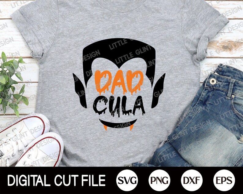 May include: A grey t-shirt with a black silhouette of a vampire with dripping orange text that reads "Dad Cula".