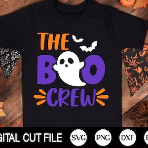 Könnte beinhalten: Ein schwarzes T-Shirt mit dem Text "THE BOO CREW" in Orange, Lila und Weiß. Ein weißer Geist mit einem lila Heiligenschein befindet sich in der Mitte des Textes. Zwei Fledermäuse befinden sich über dem Text.
