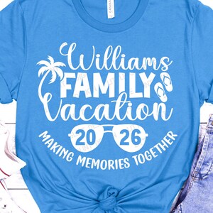 May include: A light blue t-shirt with the text "Williams FAMILY Vacation 2026 MAKING MEMORIES TOGETHER" in white. The design includes a palm tree, sunglasses, and flip-flops. The shirt is made of a soft material.