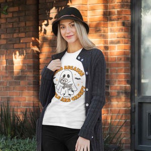 May include: White t-shirt with a graphic of a ghost holding a skeleton dog. The text on the shirt reads "Dogs because people are creepy".