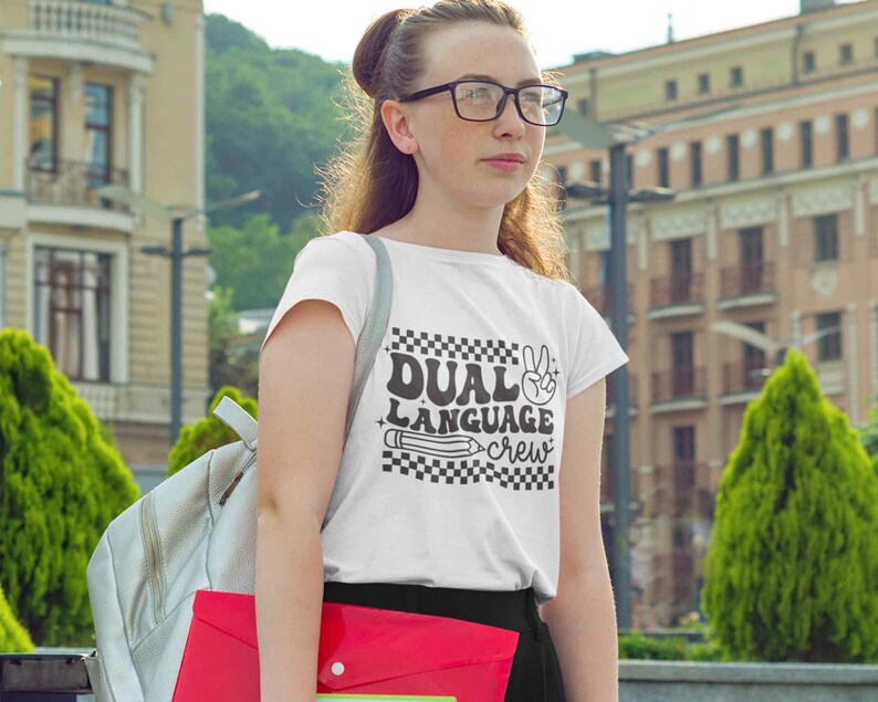 May include: White t-shirt with a black graphic that says "Dual Language Crew" with a peace sign and a pencil.