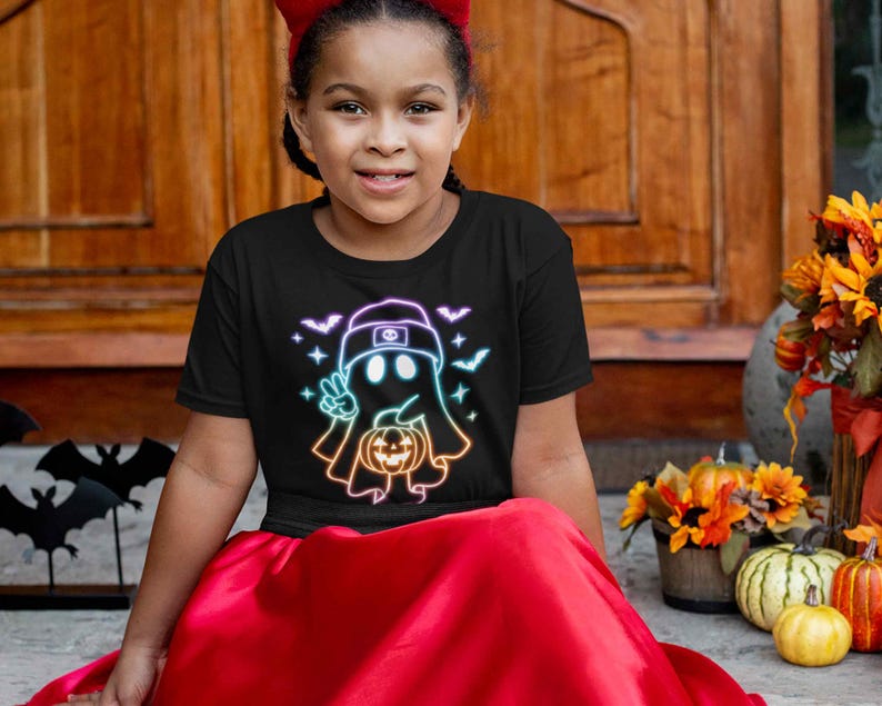 May include: A young person wearing a black t-shirt with a neon rainbow ghost holding a jack-o-lantern. The ghost is wearing a backwards baseball cap. The t-shirt is a Halloween themed design.