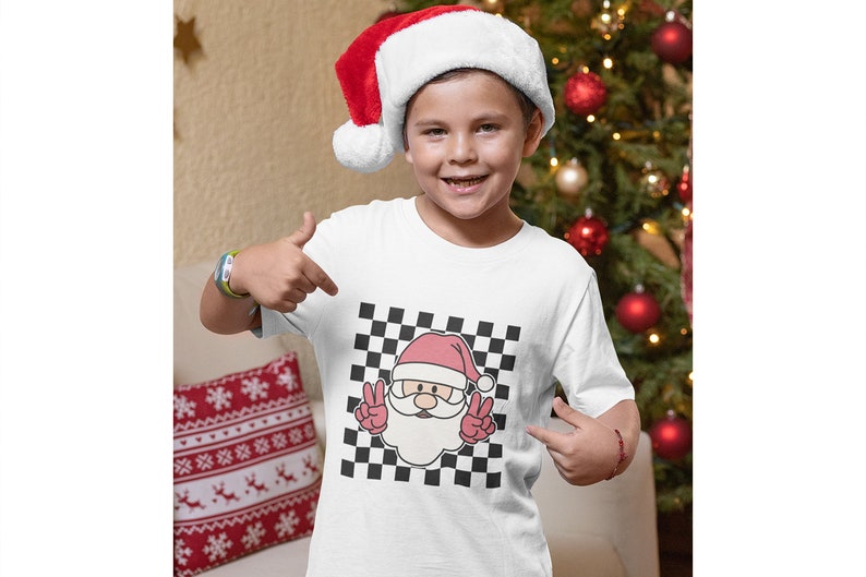 May include: White t-shirt with a black and white checkered pattern featuring a cartoon Santa Claus with a red hat and beard, making a peace sign with both hands.