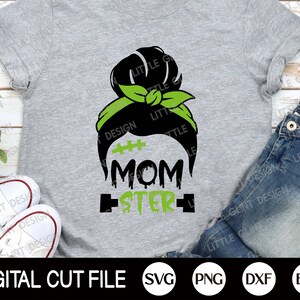 May include: A grey t-shirt featuring a black and green design of a woman's hair in a bun with a green headband. The text "Momster" is written below the hair design.