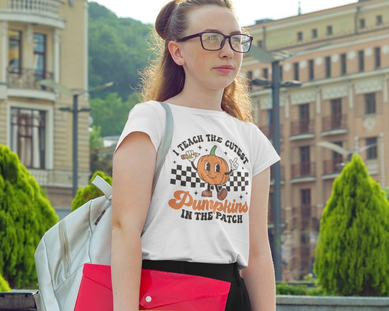 May include: White t-shirt with a graphic of a smiling pumpkin holding a pencil and the text "I teach the cutest Pumpkins in the patch".