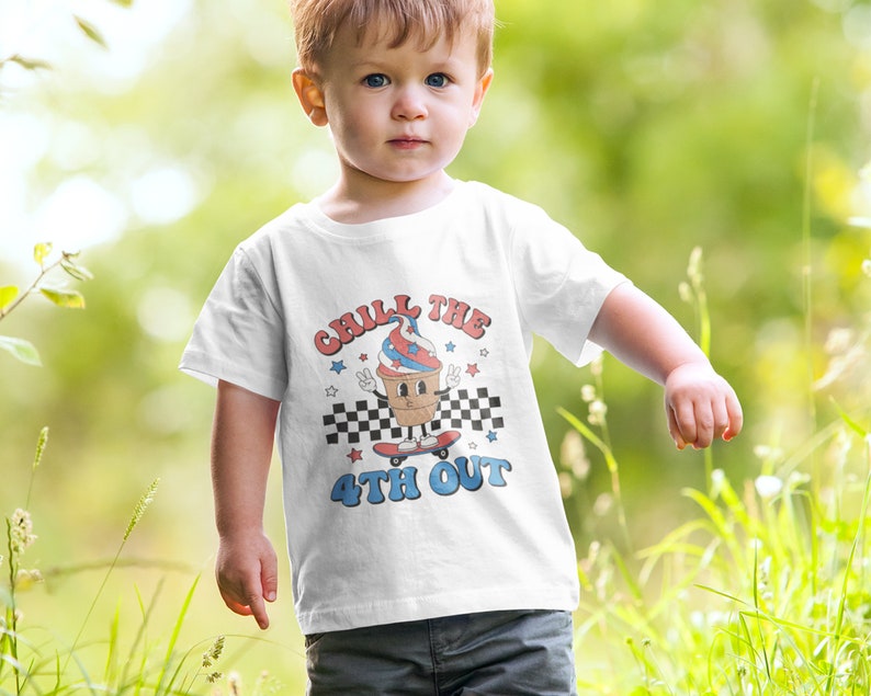May include: White t-shirt with a graphic of an ice cream cone on a skateboard. The ice cream cone is wearing a red, white, and blue hat and has a peace sign. The text on the shirt says "Chill the 4th Out".