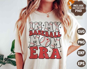 Può includere: T-shirt color crema con la scritta "IN MY BASEBALL MOM ERA" in un font retrò. Il design include palline da baseball e una pallina da baseball con un cuore. La maglietta ha un aspetto vintage e usurato.