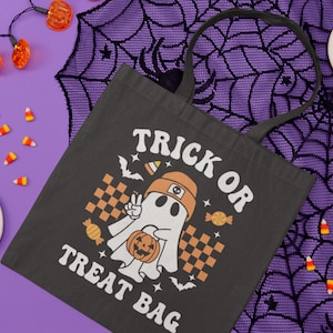 Pu&ograve; includere: Borsa tote in tela nera con un fantasma bianco che tiene una zucca e il testo "Trick or Treat Bag".