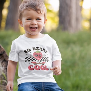 K&ouml;nnte beinhalten: Ein wei&szlig;es T-Shirt mit einem Aufdruck einer Erdbeere, die eine Sonnenbrille tr&auml;gt und Skateboard f&auml;hrt. Der Text "SO BERRY COOL" ist auf dem Shirt aufgedruckt.