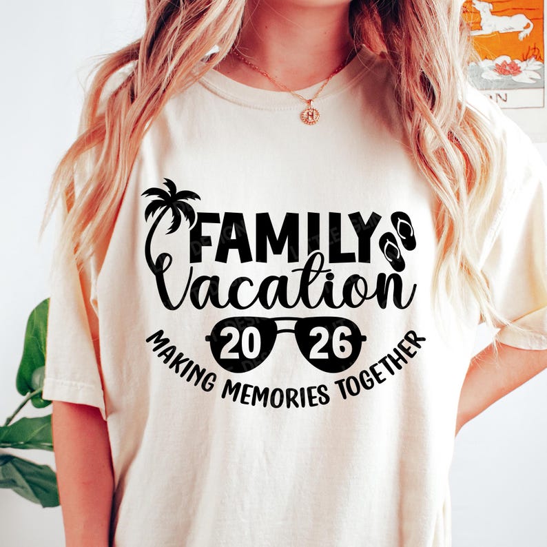 May include: Cream-colored t-shirt with a black graphic that reads "FAMILY Vacation 20 26 MAKING MEMORIES TOGETHER." The design includes a palm tree, sunglasses, and flip-flops. The shirt is a casual wear item.