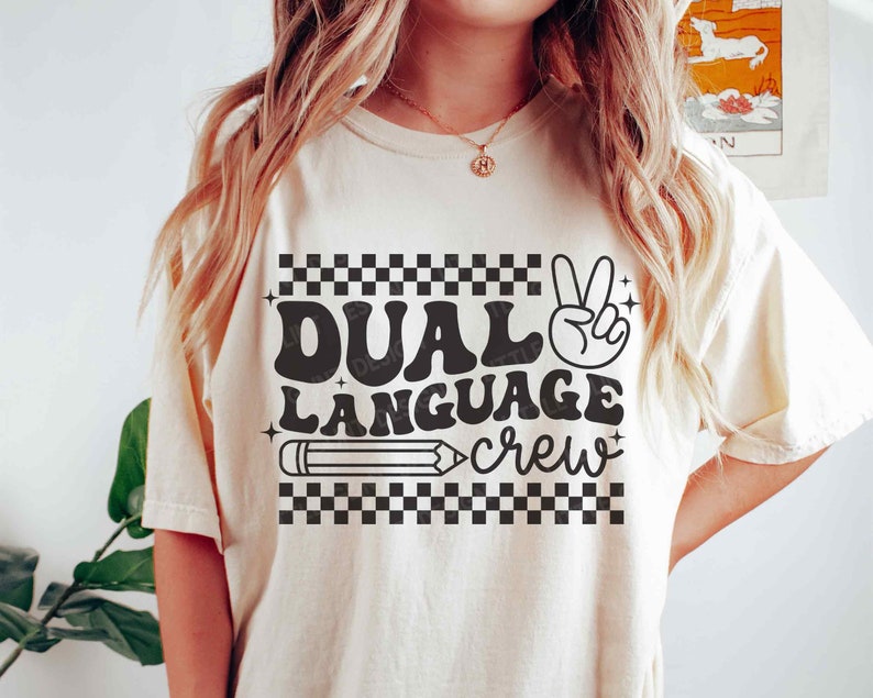 May include: A white t-shirt with black text that reads "Dual Language Crew" with a peace sign and a pencil graphic.