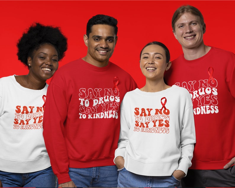 May include: Four people wearing red and white sweatshirts with the text "Say No To Drugs Say Yes To Kindness" in a retro font. Each sweatshirt features a red ribbon.