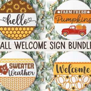 May include: Set of four round wooden signs with fall-themed designs. The signs feature the text "hello", "Farm Fresh Pumpkins", "Sweater Weather", and "Welcome". Each sign has a different fall-themed pattern.