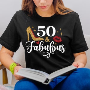 K&ouml;nnte beinhalten: Ein schwarzes T-Shirt mit goldfarbenem Glitzer-Schriftzug, auf dem "50 & Fabulous" steht, mit einem goldenen Glitzer-High-Heel-Schuh und einem roten Glitzer-Lippenabdruck.