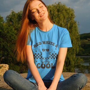May include: A woman wearing a blue t-shirt with a graphic of a cartoon character skateboarding and the text "Red White & Cool".