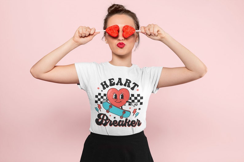 K&ouml;nnte beinhalten: Wei&szlig;es T-Shirt mit einem roten Herz-Motiv, das Skateboard f&auml;hrt, und dem Text "HEART BREAKER" in einer Retro-Schrift.