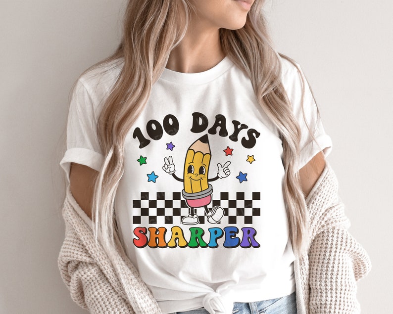 May include: White t-shirt with a colorful graphic of a pencil with a smiling face and the text "100 Days Sharper".
