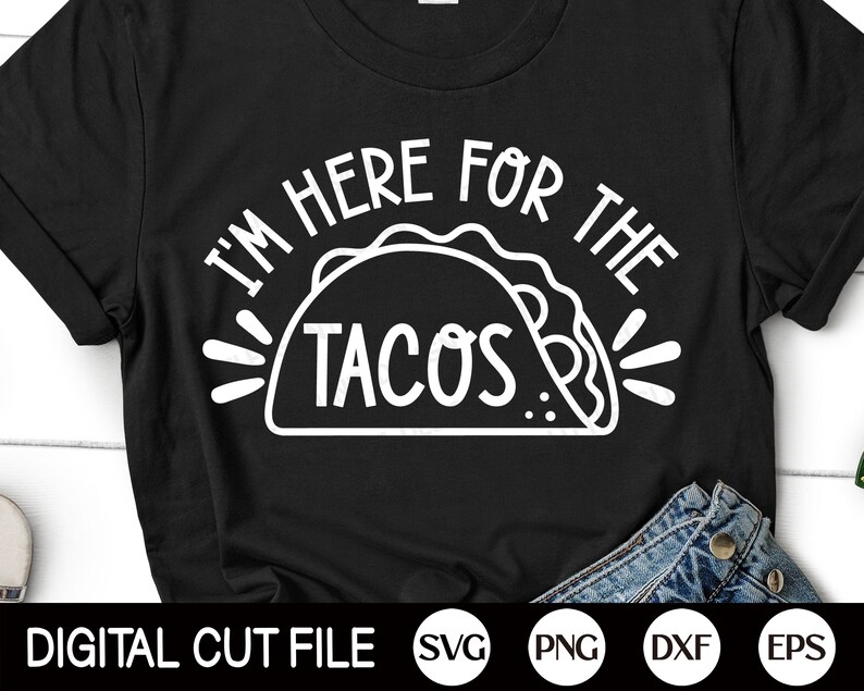 Puede incluir: Camiseta negra con un gr&aacute;fico blanco que dice "I'M HERE FOR THE TACOS" encima de una ilustraci&oacute;n de taco. La parte inferior de la camiseta muestra una porci&oacute;n de jeans azules. Las palabras "DIGITAL CUT FILE" est&aacute;n en la parte inferior.