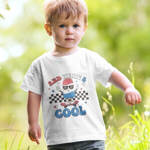 May include: White t-shirt with a red, white, and blue cartoon character wearing sunglasses and skateboarding. The text "Red White & Cool" is printed on the shirt.