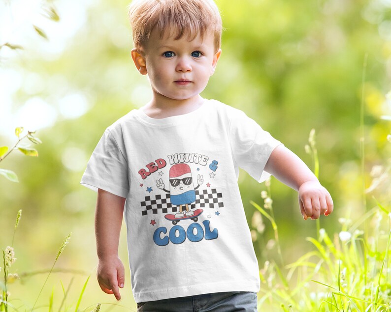 May include: White t-shirt with a red, white, and blue cartoon character wearing sunglasses and skateboarding. The text "Red White & Cool" is printed on the shirt.