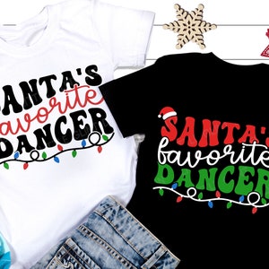 May include: Two Christmas-themed t-shirts with the text "Santa's favorite dancer" in a retro font. The shirts are white and black with red and green accents. The text is surrounded by a string of Christmas lights.