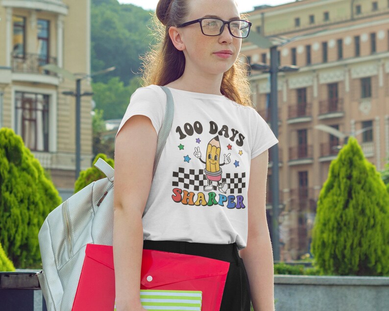 May include: White t-shirt with a graphic of a cartoon pencil with the text "100 Days Sharper".