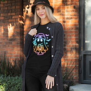 May include: A black t-shirt featuring a rainbow outline of a ghost holding a pumpkin. The ghost is wearing a hat. The design's background includes bats and stars.