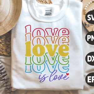 Puede incluir: Una sudadera blanca con un gr&aacute;fico de arco&iacute;ris que dice "love is love" con un peque&ntilde;o coraz&oacute;n rojo.