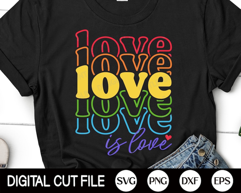 Puede incluir: Camiseta negra con un dise&ntilde;o de arco&iacute;ris que dice "Love is Love" con un peque&ntilde;o coraz&oacute;n rojo.
