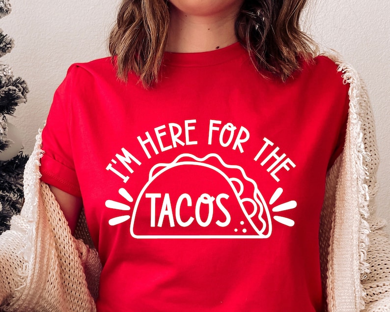 Puede incluir: Camiseta roja con el texto blanco "I'M HERE FOR THE TACOS" y un gr&aacute;fico de taco. La camiseta es de manga corta.