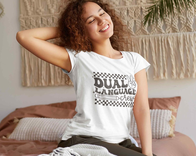 May include: White t-shirt with a black and white checkered design and the text "Dual Language Crew" in a retro font. A peace sign and a pencil are also included in the design.