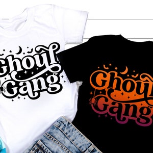 May include: Two t-shirts with the text "Ghoul Gang" in a spooky font. One shirt is white with black text and the other is black with orange and pink text.
