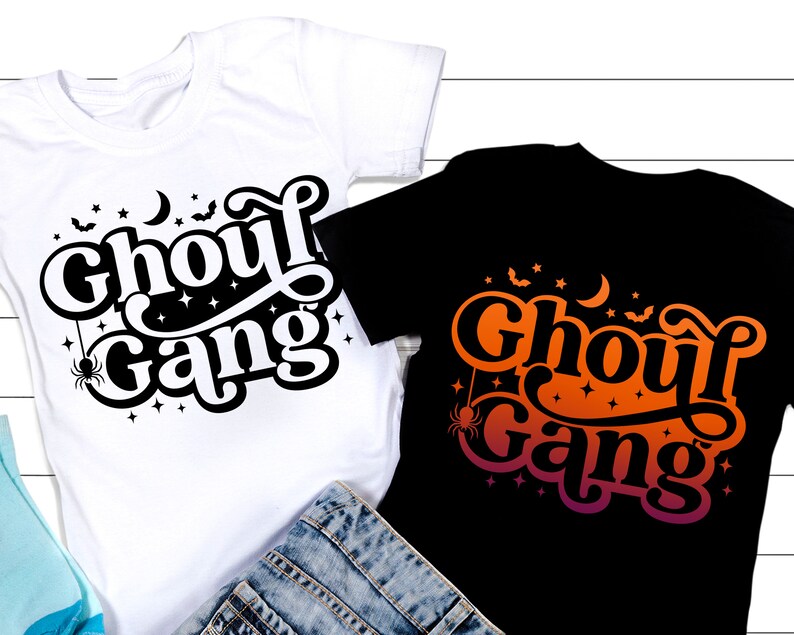 May include: Two t-shirts with the text "Ghoul Gang" in a spooky font. One shirt is white with black text and the other is black with orange and pink text.