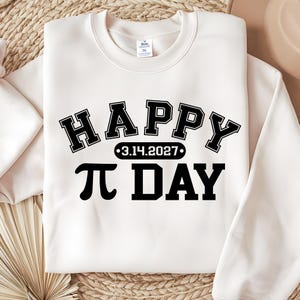 Pu&ograve; includere: Felpa color crema con le parole "HAPPY" e "&pi; DAY" in grassetto nero, in stile collegiale. La data "3.14.2027" &egrave; centrata tra le parole. La felpa &egrave; realizzata in un materiale morbido.