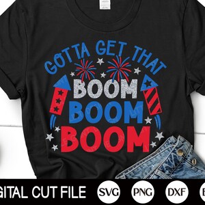 Op de afbeelding: Zwart T-shirt met de tekst "Gotta Get That Boom Boom Boom" in rood, wit en blauw met vuurwerk- en vonkenafbeeldingen.