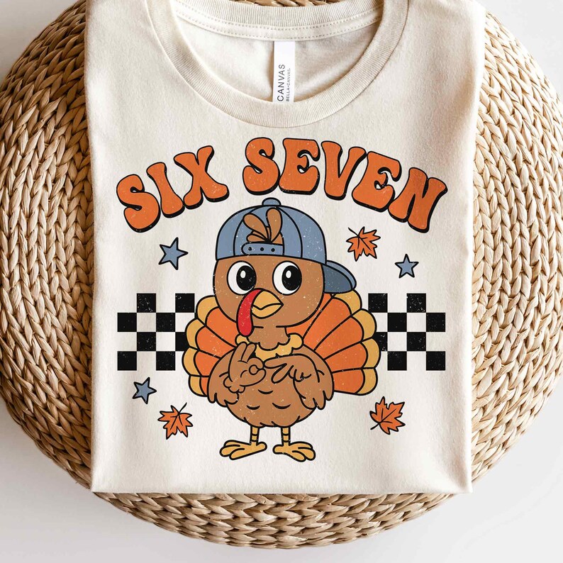 Pu&ograve; includere: T-shirt color crema con un tacchino dei cartoni animati con un berretto blu. Il tacchino ha piume arancioni e marroni e fa il segno della pace. Il testo "SIX SEVEN" &egrave; in arancione, con un lettering in stile retr&ograve; sopra il tacchino. Motivo a scacchiera in bianco e nero in basso.