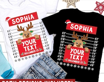 May include: Two white and black t-shirts with a red and white Christmas design. The design features a reindeer with a red Santa hat peeking over a red sign that says "Your Text" and "December 25". The shirts also have a white line with measurements in inches and the name "Sophia" printed on them.