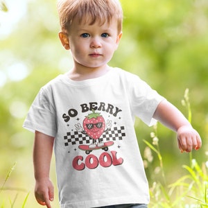 K&ouml;nnte beinhalten: Ein wei&szlig;es T-Shirt mit einer Comic-Erdbeere, die eine Sonnenbrille tr&auml;gt und Skateboard f&auml;hrt. Der Text "SO BERRY COOL" ist auf das Shirt gedruckt.