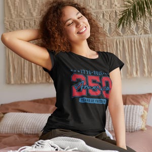 May include: A black t-shirt with a red and blue graphic commemorating 250 years of America. The design includes the text "1776-2026" and "250 America Years of Freedom". The shirt is worn by a person.