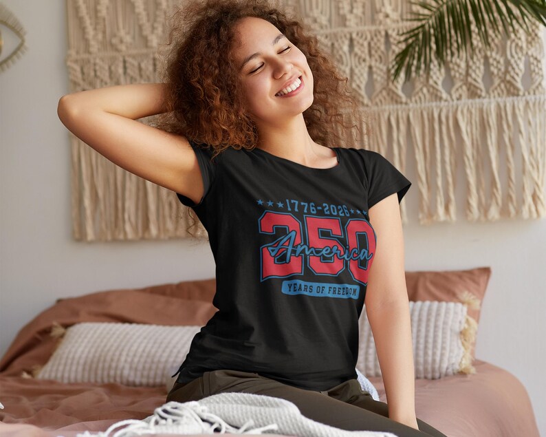 May include: A black t-shirt with a red and blue graphic commemorating 250 years of America. The design includes the text "1776-2026" and "250 America Years of Freedom". The shirt is worn by a person.