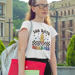May include: White t-shirt with a graphic of a cartoon pencil with the text "100 Days Sharper".