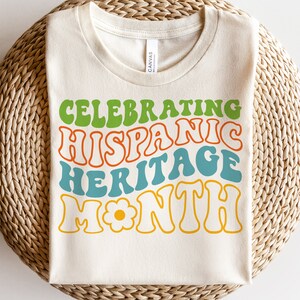May include: A white t-shirt with the text "Celebrating Hispanic Heritage Month" in a retro, colorful font. The text is in green, orange, blue, and yellow.