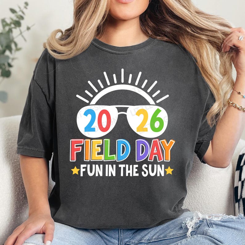 May include: Dark gray t-shirt with a colorful graphic. The design features the numbers "2026" in sunglasses, the words "FIELD DAY" in rainbow colors, and "FUN IN THE SUN" with star accents. The shirt has a casual, relaxed fit.