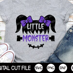 May include: A purple and black graphic design on a grey t-shirt that says "Little Monster" with dripping purple paint and a stitched-up mouth. The design includes two purple bows on top of the head.