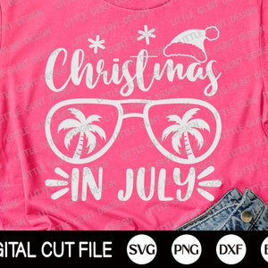 May include: Pink t-shirt with white text that reads "Christmas in July" with a pair of sunglasses with palm trees inside the lenses. The text is in a fun, whimsical font.