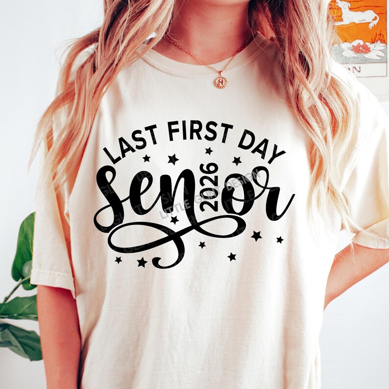 May include: Cream-colored t-shirt with the text "LAST FIRST DAY SENIOR 2026" in black script and block letters, with star accents. The shirt is a casual style.
